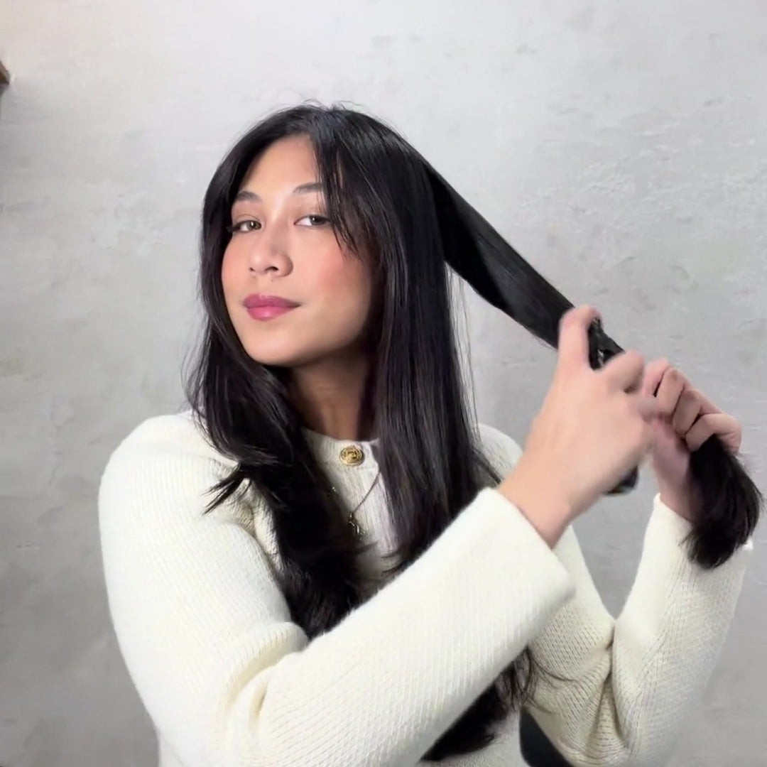 A woman dividing her long, dark hair into sections to ensure even distribution of a professional heat protectant spray before styling